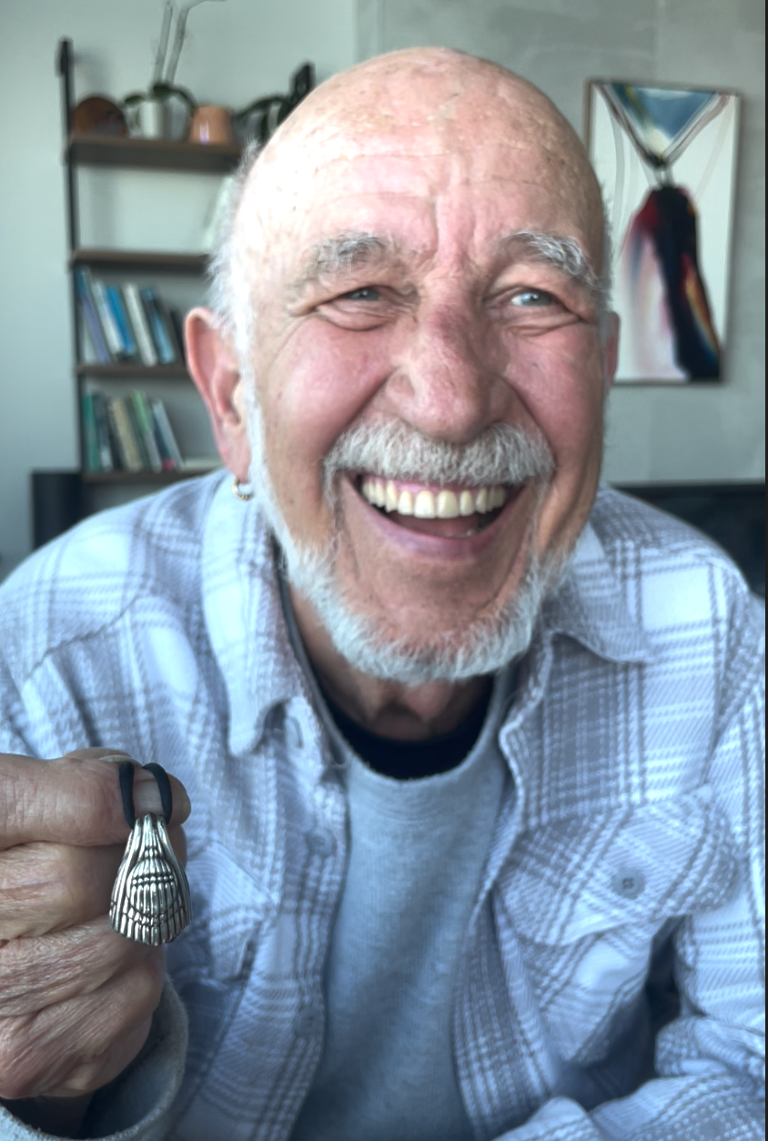 bell maker in a grey striped shirt holding the sterling silver jewelry bell necklace, the aurora